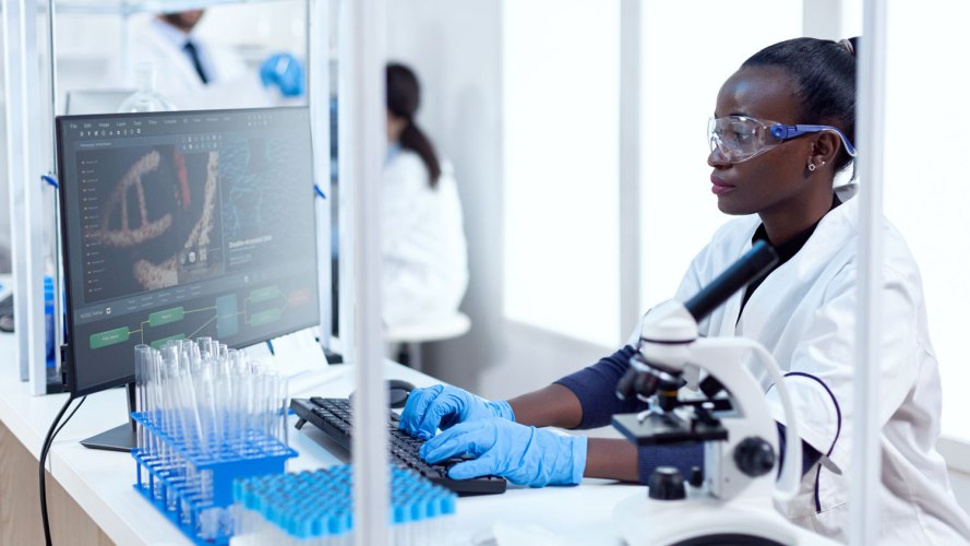 Mujer científica en un entorno clínico frente a una computadora en un laboratorio que trabaja con información de ensayos clínicos descentralizados