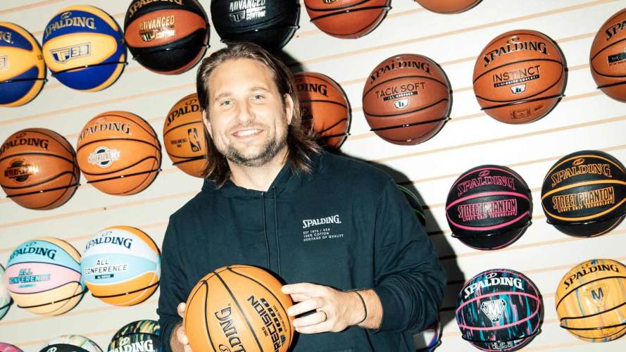 persona sosteniendo una pelota de baloncesto frente a una pared cubierta de pelotas de baloncesto